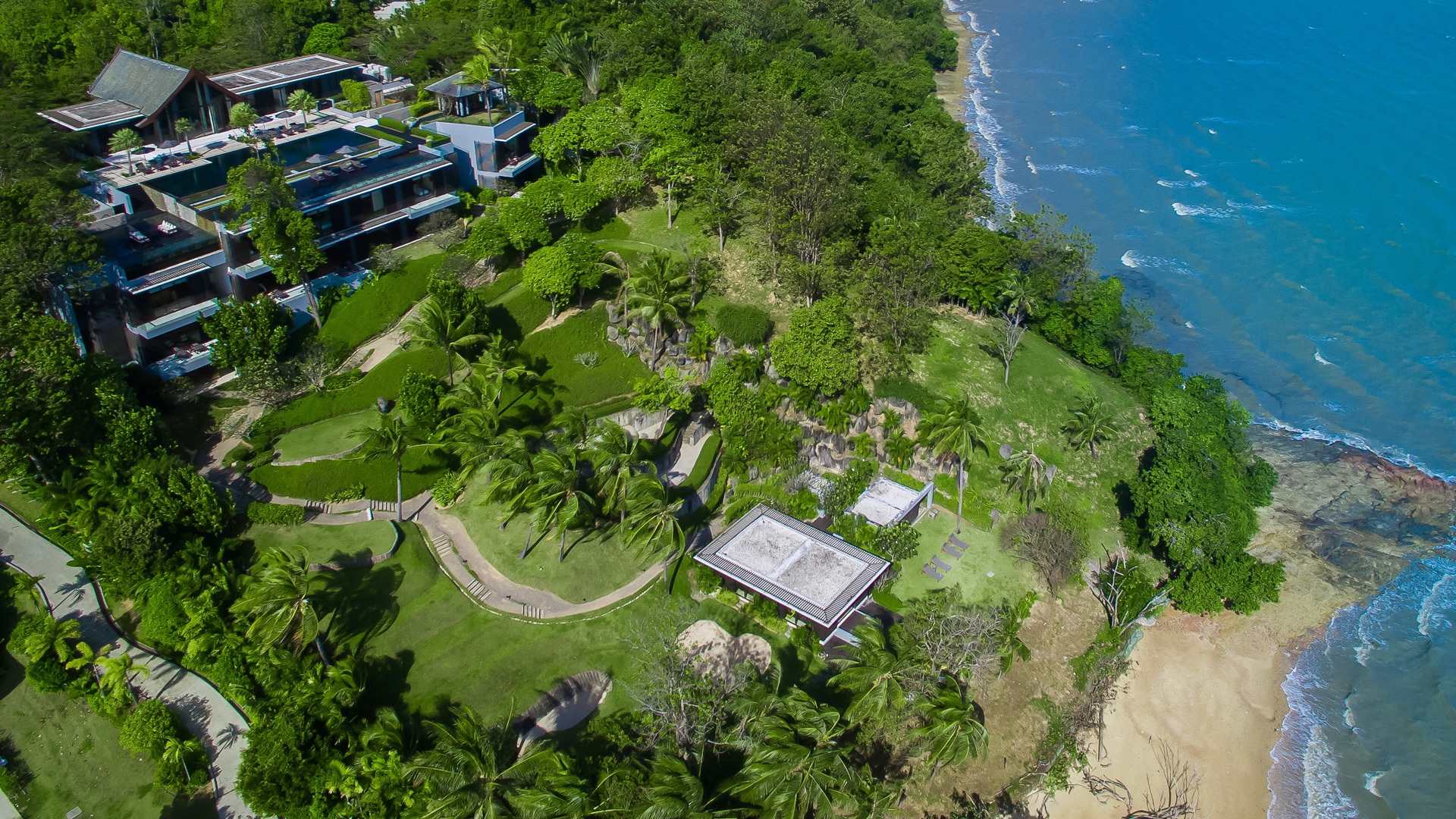 Villa Sawarin from above: pavilions and pools stepping down a green headland to a lone beach house and the sea.